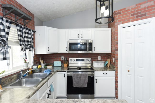 Kitchen featuring a sink, vaulted ceiling, white cabinetry, a textured ceiling, and appliances with stainless steel finishes | Image 15