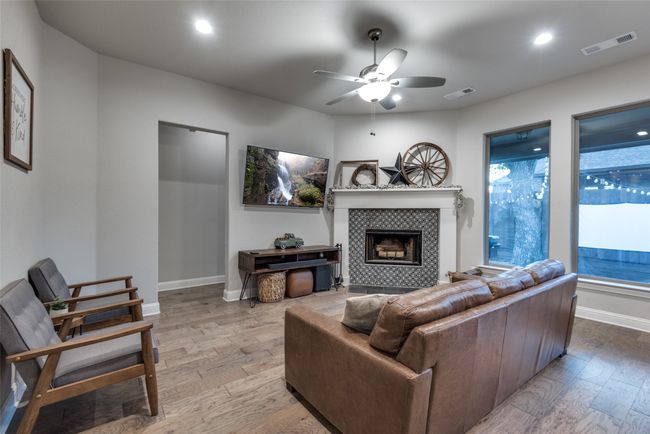 Living room featuring a ceiling fan, wood finished floors, a tile fireplace, baseboards, and visible vents | Image 11