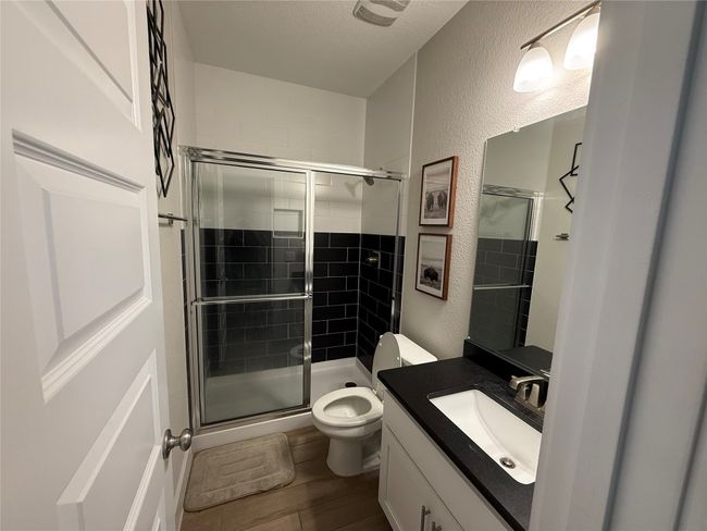 Full bathroom featuring toilet, a textured wall, a stall shower, vanity, and wood finished floors | Image 4