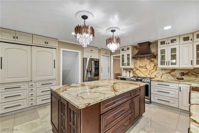 Kitchen with tasteful backsplash, stainless steel appliances, an inviting chandelier, custom exhaust hood, and dark brown cabinetry | Image 3