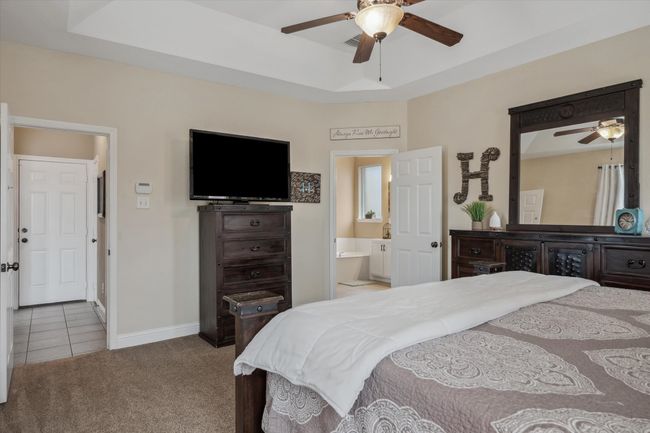Tiled bedroom featuring a raised ceiling, carpet flooring, ceiling fan, ensuite bath, and baseboards | Image 16