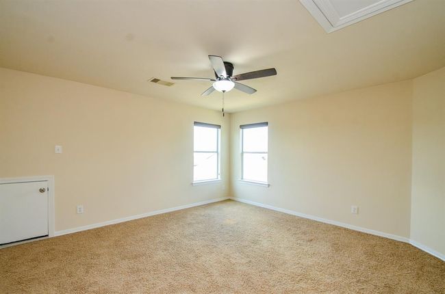Spacious game room with neutral walls and carpet, featuring a ceiling fan and two windows for natural light. | Image 24