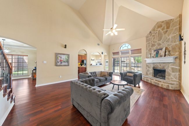 Living room with a fireplace, stairway, a ceiling fan, dark wood-type flooring, and arched walkways | Image 5