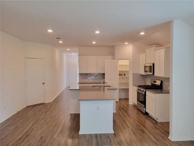 Kitchen featuring appliances with stainless steel finishes, a kitchen island with sink, dark wood finished floors, backsplash, and recessed lighting | Image 7