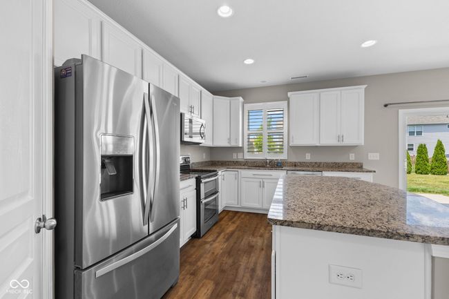 Kitchen with appliances with stainless steel finishes, white cabinets, recessed lighting, dark wood-style floors, and dark stone counters | Image 11