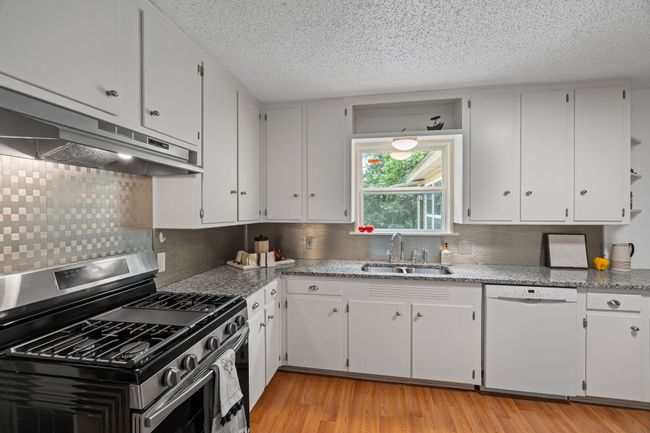 Kitchen featuring stainless steel gas range, dishwasher, under cabinet range hood, backsplash, and white cabinets | Image 9