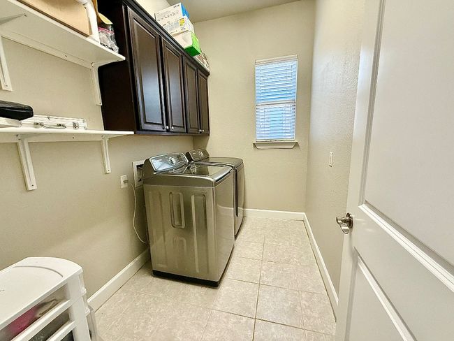 Laundry area featuring washing machine and dryer, cabinet space, light tile patterned floors, and baseboards | Image 32