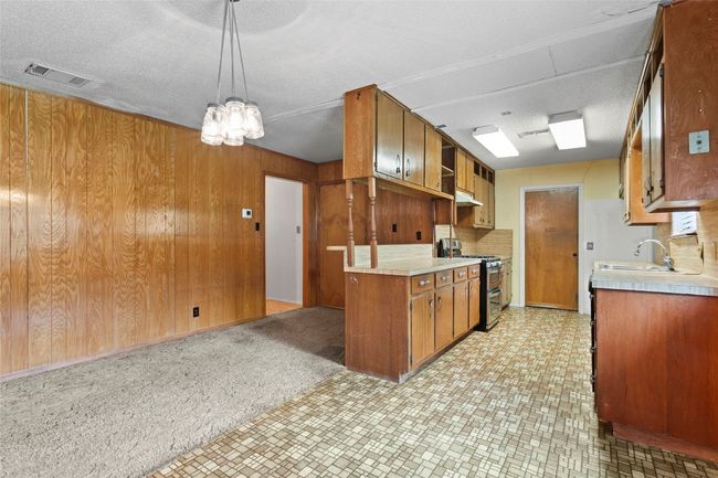 Kitchen featuring double oven range, light countertops, brown cabinets, under cabinet range hood, and wood walls | Image 6