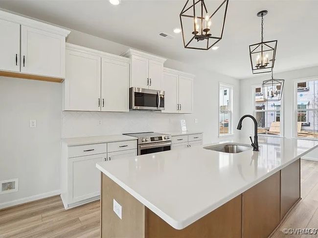 Kitchen featuring stainless steel appliances, a chandelier, white cabinets, light wood-style floors, and a spacious island | Image 16