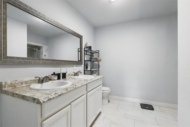 Bathroom featuring marble look tiles, baseboards, toilet, double vanity, and a shower with curtain | Image 27