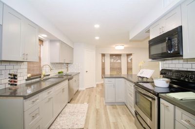 This is a modern, well-lit kitchen featuring gray cabinets, stainless steel appliances, white subway tile backsplash, and wood-look flooring. It has ample counter space and a fresh, clean design. | Image 2