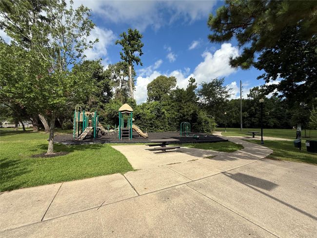 Charming neighborhood park with a playground surrounded by lush greenery. It features play structures, picnic tables, and a paved walkway, ideal for family outings and outdoor activities. | Image 32