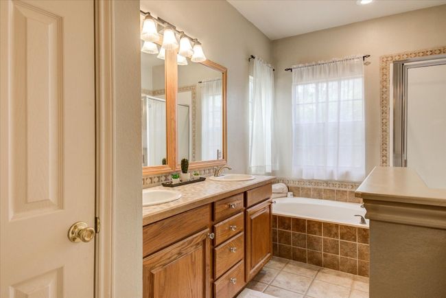 Primary bathroom features a double vanity, tile patterned flooring, an separate shower, a soaking tub, linen closet and a walk-in closet. | Image 11