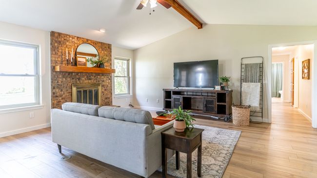 Living area with a fireplace, light wood finished floors, lofted ceiling with beams, and ceiling fan | Image 15
