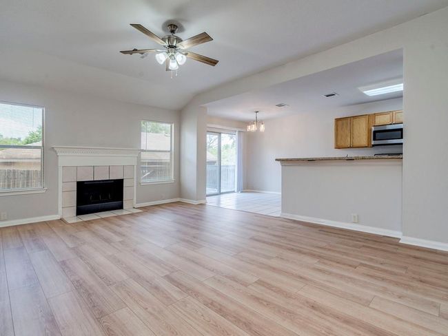 Unfurnished living room with light wood-style floors, a ceiling fan, a chandelier, and a tiled fireplace | Image 8