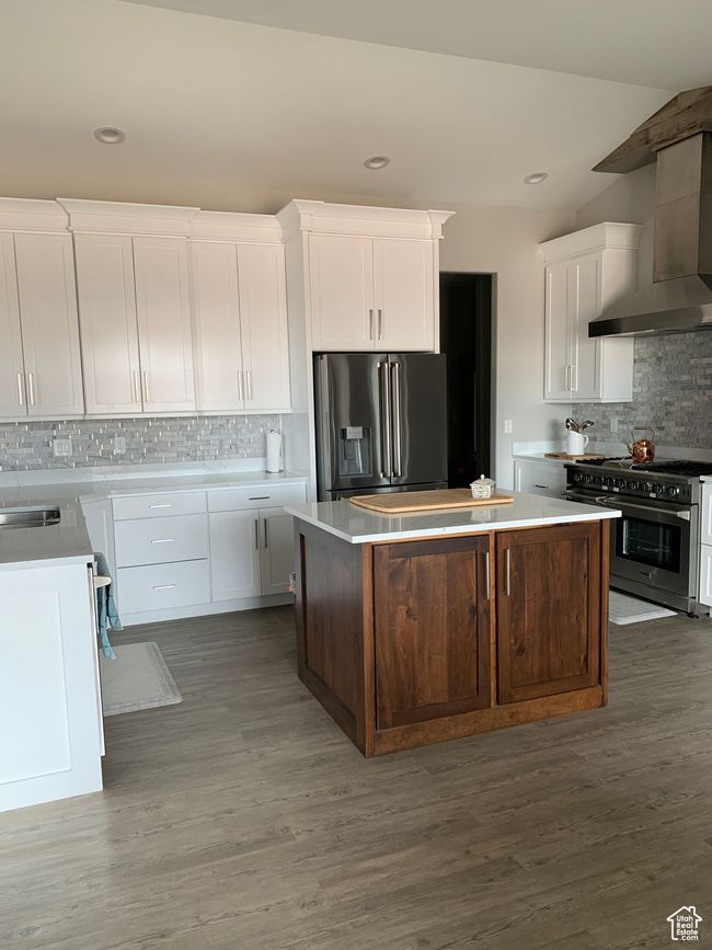 Kitchen with white cabinets, a kitchen island, wood finished floors, stainless steel appliances, and wall chimney range hood | Image 7