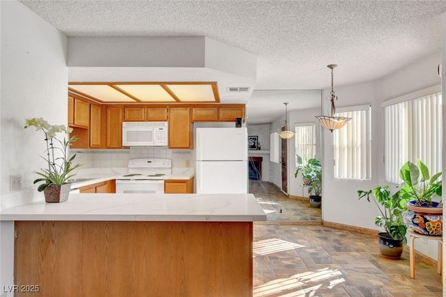 Kitchen with white appliances, a peninsula, visible vents, decorative light fixtures, and baseboards | Image 16