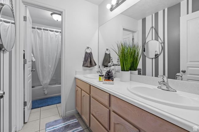 Full bath featuring double vanity, a sink, tile patterned floors, and shower / tub combo with curtain | Image 33