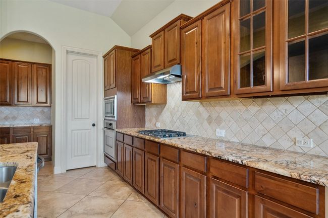 Kitchen featuring tasteful backsplash, light stone countertops, light tile patterned flooring, glass insert cabinets, and vaulted ceiling | Image 21
