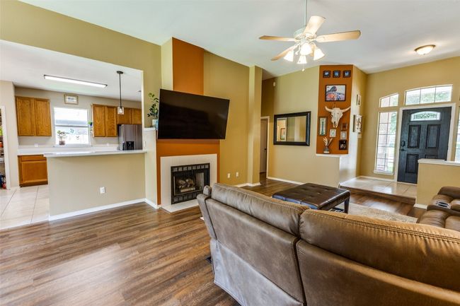 Living area with wood finished floors, a tiled fireplace, ceiling fan, and baseboards | Image 7