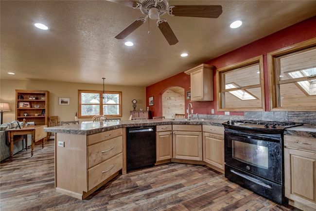 Kitchen featuring black appliances, light brown cabinets, a peninsula, tile counters, and dark wood-type flooring | Image 16