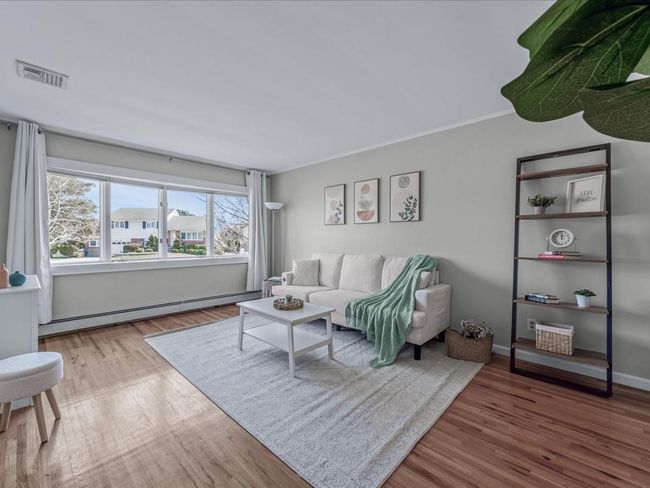 Living area featuring wood finished floors, baseboards, visible vents, a baseboard heating unit, and ornamental molding | Image 4