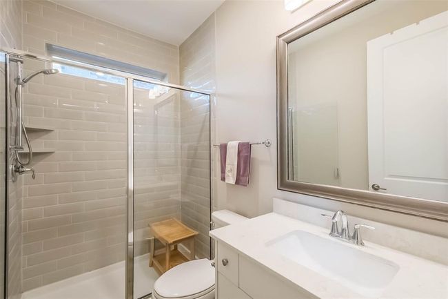 The guest suite bathroom features a large walk-in shower with window, quartz counters and framed mirror. | Image 22