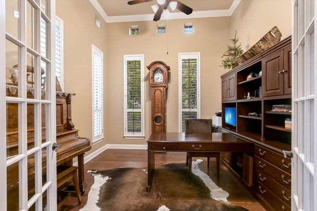 Office featuring ceiling fan, crown molding, and dark wood flooring behind French Doors just off the entry foyer. | Image 6