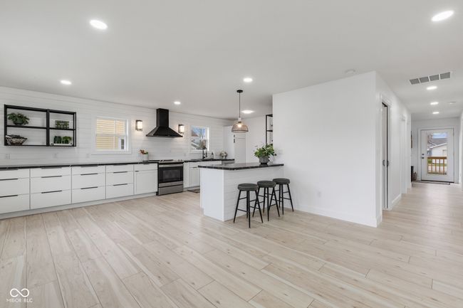 kitchen with a breakfast bar, wall chimney range hood, stainless steel electric range oven, white cabinets, and visible vents | Image 22