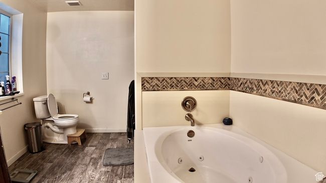 Full bathroom with visible vents, baseboards, toilet, a tub with jets, and wood finished floors | Image 54