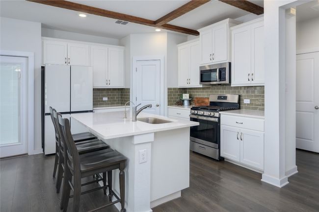 Kitchen with stainless steel appliances, beam ceiling, dark wood finished floors, recessed lighting, and a center island with sink | Image 6