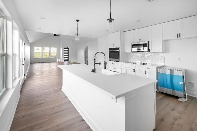 Kitchen with backsplash, light wood-type flooring, a sink, stainless steel appliances, and white cabinetry | Image 9