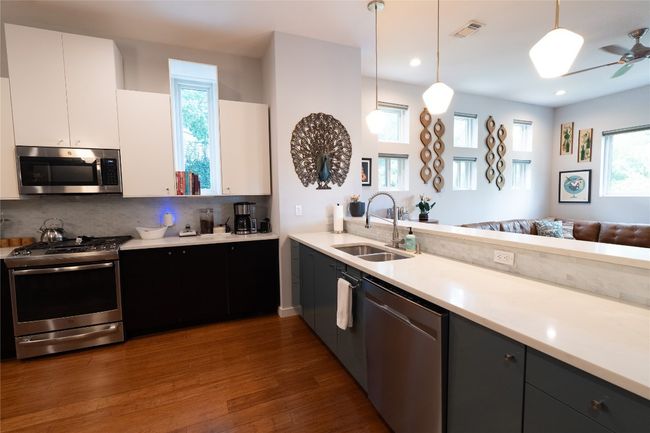 Kitchen with appliances with stainless steel finishes, wood finished floors, white cabinetry, light countertops, and backsplash | Image 26