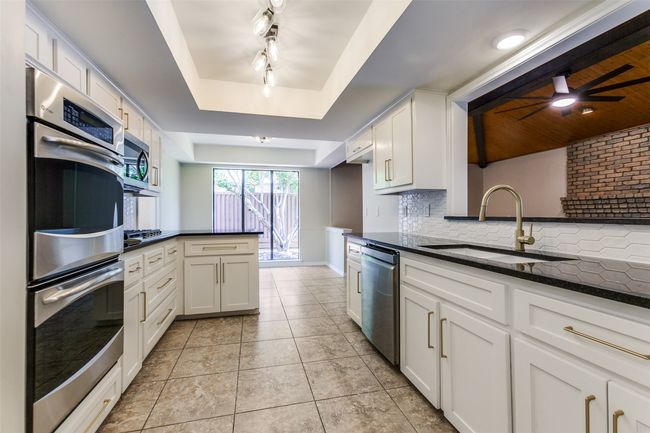 Kitchen with appliances with stainless steel finishes, a tray ceiling, a peninsula, tasteful backsplash, and white cabinetry | Image 16