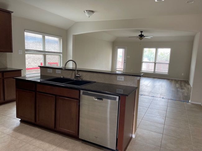 Kitchen with dishwasher, vaulted ceiling, light tile patterned floors, a ceiling fan, and a kitchen island with sink | Image 7