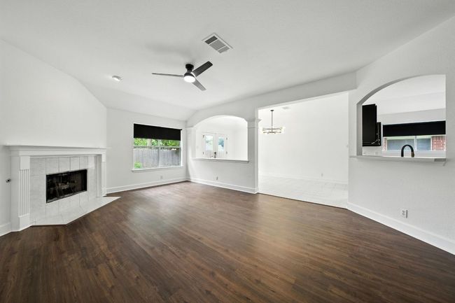 Living room with lofted ceiling, a ceiling fan, a tile fireplace, wood finished floors, and arched walkways | Image 7