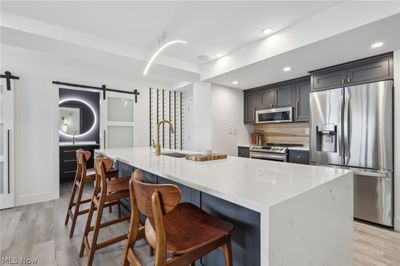 Kitchen featuring a barn door, stainless steel appliances, light hardwood / wood-style flooring, and a center island with sink | Image 3