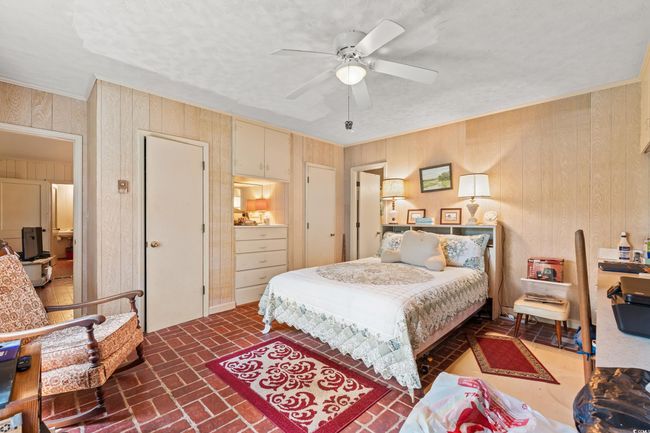 Bedroom featuring brick flooring, wood walls, crown molding, and ceiling fan | Image 8
