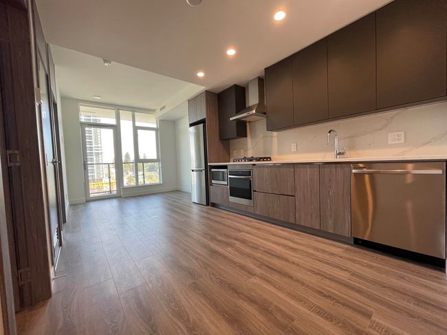 Kitchen with modern cabinets, stainless steel appliances, wall chimney exhaust hood, light countertops, and wood finished floors | Image 9