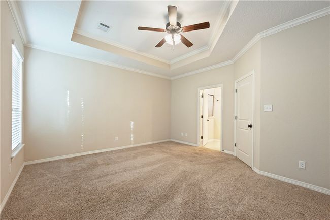 Empty room with a raised ceiling, ceiling fan, carpet flooring, and crown molding | Image 12