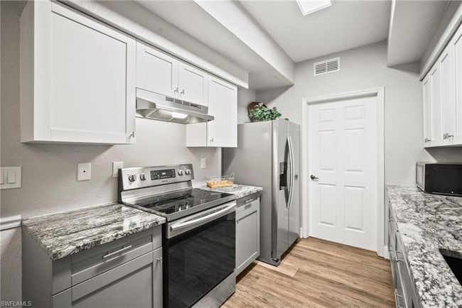 Kitchen with light wood-type flooring, stainless steel appliances, under cabinet range hood, visible vents, and white cabinets | Image 10