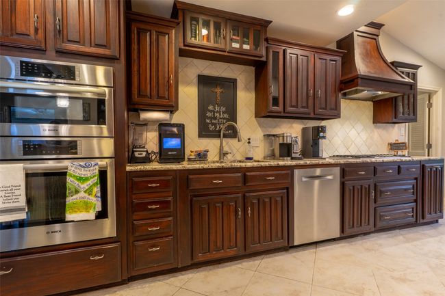 Kitchen featuring stainless steel appliances, custom range hood, tasteful backsplash, a sink, and light stone countertops | Image 9