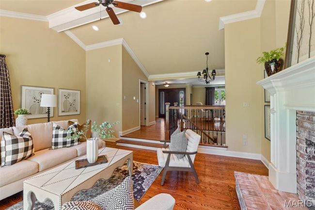 Living room featuring wood finished floors, ceiling fan, a chandelier, crown molding, and a fireplace | Image 9