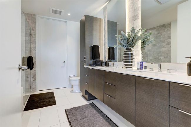 Bathroom with double vanity, tile patterned floors, toilet, and a tile shower | Image 13