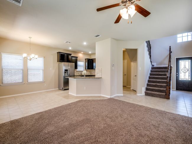 Unfurnished living room featuring light tile patterned floors, light carpet, ceiling fan with notable chandelier, visible vents, and stairway | Image 5