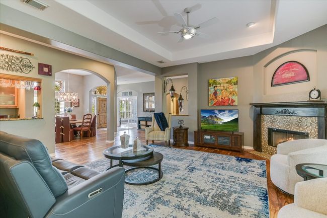 Living area with arched walkways, a ceiling fan, a tiled fireplace, wood finished floors, and baseboards | Image 11