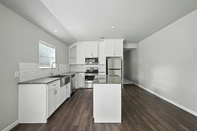 Kitchen featuring white cabinetry, dark stone countertops, open shelves, appliances with stainless steel finishes, and recessed lighting | Image 5