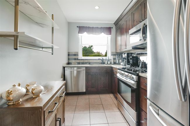Kitchen with stainless steel appliances, a sink, decorative backsplash, light tile patterned floors, and dark brown cabinets | Image 4