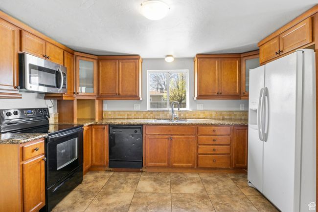 Kitchen with glass insert cabinets, brown cabinetry, black appliances, light stone counters, and a sink | Image 28