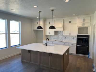 Kitchen featuring pendant lighting, light stone counters, sink, an island with sink, and white cabinets | Image 3